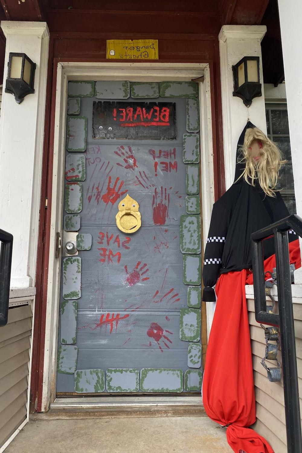 A dorm house door made up to appear like a dungeon with handprints and messages in blood.